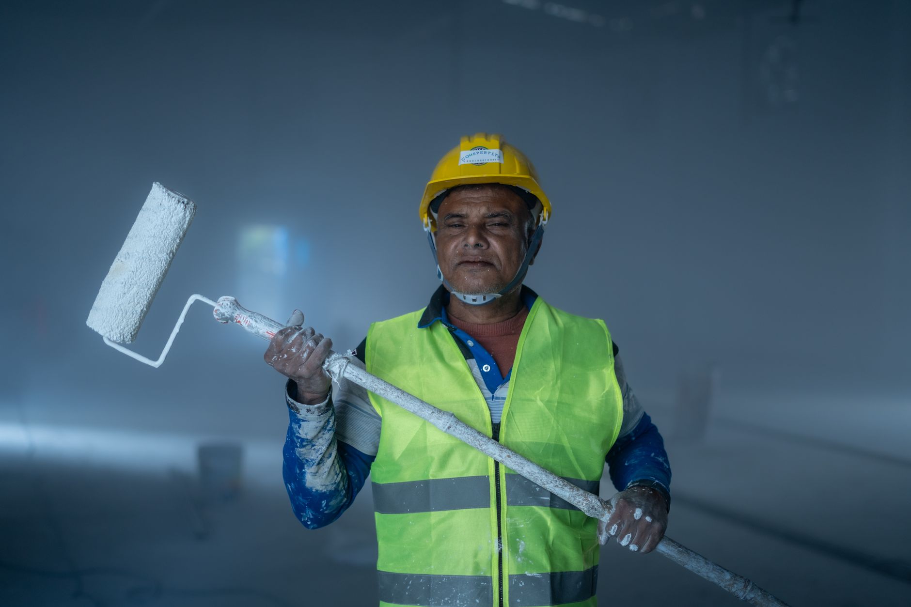 A construction worker wearing a helmet and safety vest holding a paint roller inside an unfinished in Rancho Cucamonga, CA